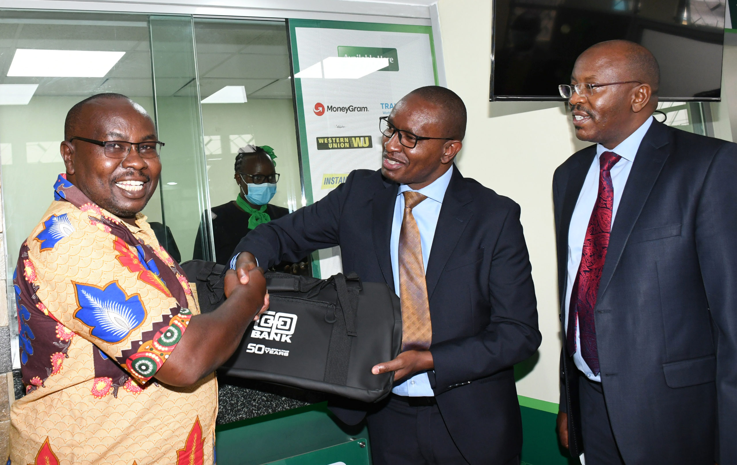 Director Retail & Business Banking William Ndumia presents a gift to Mr. who was the first client to open an account after the official opening of Co-op Kamulu branch Mr Joseph Kimathi Ndegwa . Looking on is the bank's Head of Branch Banking Peter Kirugu.